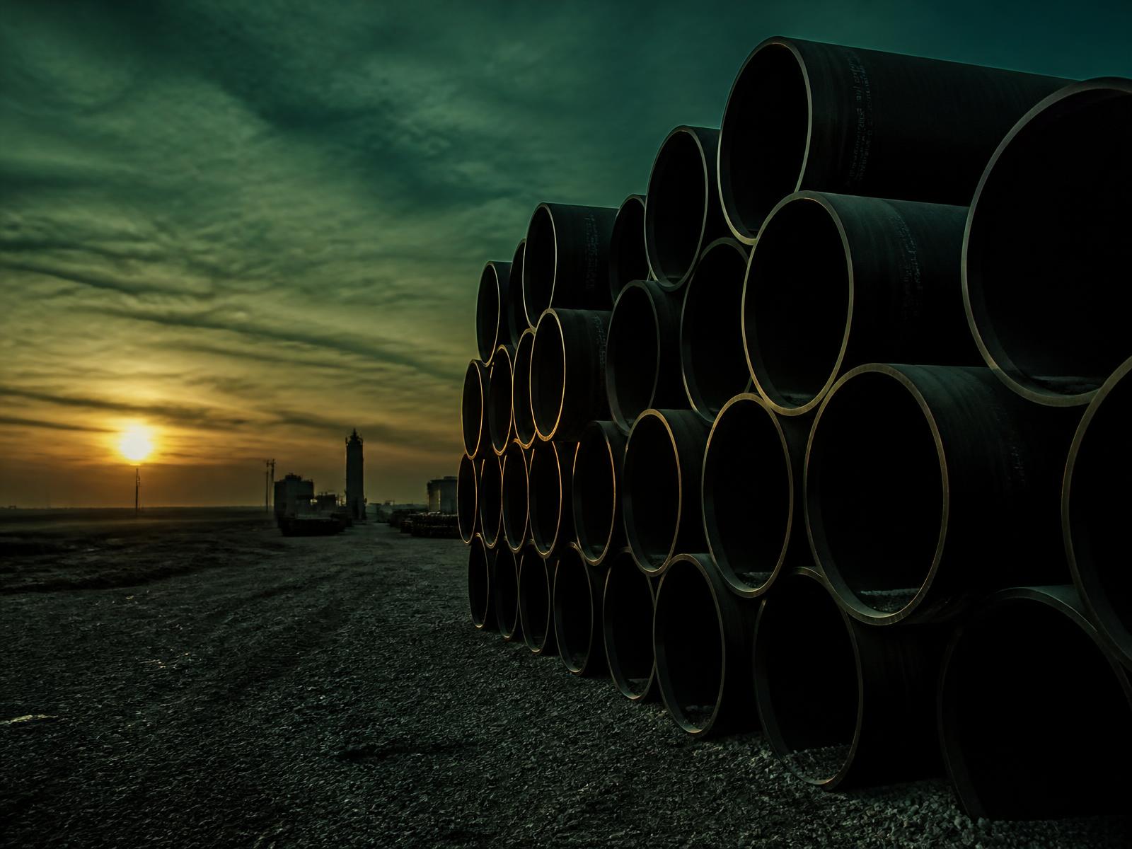 Stacked black HDPE pipe sections in an industrial yard at dusk